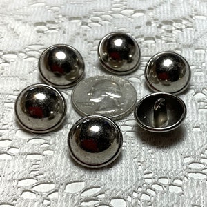 May include: Six silver-toned dome-shaped buttons with a raised rim. The buttons have a smooth, shiny finish.