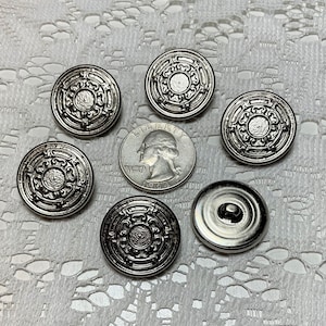 May include: Six silver-toned buttons with an ornate design. The buttons are round and have a raised center. The buttons are arranged in a circle around a silver-toned quarter.