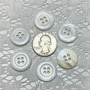May include: Six white mother of pearl buttons with four holes each. The buttons are arranged in a circle around a US quarter.