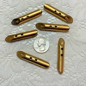 May include: Five gold-colored metal buttons with two holes each. The buttons are in various shapes and sizes, and are arranged on a white lace background.