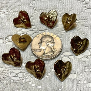 May include: Ten gold-colored heart-shaped buttons with a raised design. The buttons have a hole in the top for sewing.