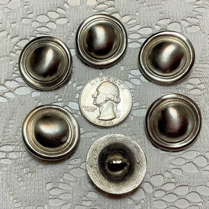 以下が含まれることがあります： ドーム型の隆起した形状と滑らかで光沢のある仕上げを施した、銀色の金属製のボタンが6つあります。ボタンは、アメリカの25セント硬貨の周りに円形に配置されています。