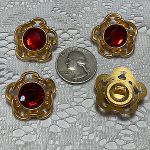 May include: Four gold-toned buttons with red rhinestone centers. The buttons have a decorative, ornate design.