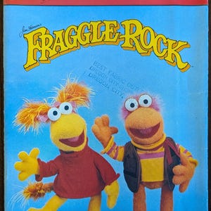 May include: A vintage Butterick craft pattern featuring the Fraggles characters Red and Gobo. The cover is blue and red, with the text "FRAGGLE ROCK" in yellow. The pattern number is 3855.
