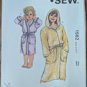 May include: A Kwik Sew pattern envelope 1562 for sizes 4-5-6-7. The front shows two illustrations: a child in a light purple striped robe with ruffled trim and a child in a yellow hooded robe with a tie belt and pockets. Includes text and barcode.
