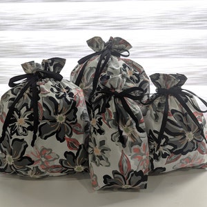 May include: Four fabric drawstring bags with floral patterns in shades of gray, black, and pink. The bags have black ribbon ties.