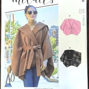 May include: McCall's sewing pattern featuring a hooded cape with tie closure. The pattern includes multiple view options and simple instructions. The model is wearing a brown cape with a matching tie. The pattern is designed and printed in the USA.