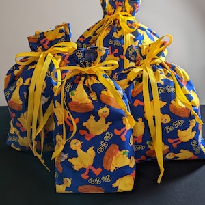 May include: Four drawstring gift bags in varying sizes. The bags are made of blue fabric patterned with yellow Big Bird characters and the words "Big Bird". Each bag is tied with a yellow ribbon.