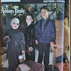 May include: A Simplicity Costumes sewing pattern envelope for The Addams Family, number 7991, size A (SM-LG). The cover features illustrations of four characters in costumes, including a dark robe, a black dress, a purple jacket, and a fur suit.