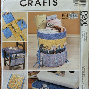 May include: A McCall's Crafts P208 sewing pattern envelope featuring illustrations of fabric organizers. The designs include a hanging basket, a chair caddy, a folding case, and a machine mat, all made from floral and patterned blue and yellow fabric.