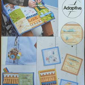May include: Simplicity R11470 Adaptive sewing pattern envelope featuring sensory lap pads and accessories. The design includes various fabric squares with tactile elements like buttons, ribbons, tassels, and clear pockets, intended for sensory stimulation.