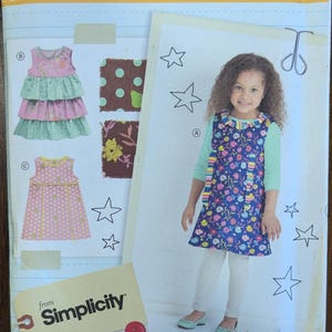 May include: A sewing pattern for children's dresses. The pattern features a girl wearing a blue floral dress. The pattern includes different dress styles and fabric swatches. The text on the pattern reads "little lisette" and "Simplicity".