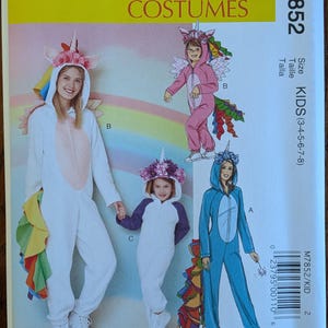 May include: McCall's Costumes M7852 sewing pattern envelope for kids sizes 3-8. The cover features illustrations of hooded unicorn jumpsuits in white, pink, and blue, each with a horn, floral headpiece, and a colorful rainbow tail attached.