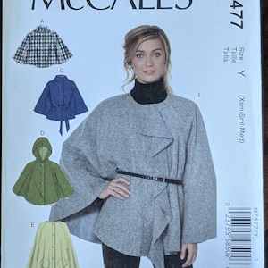 May include: McCall's sewing pattern M7477. The pattern features a woman wearing a gray cape with a black belt. The pattern also shows illustrations of different cape styles in various colors, including blue, green, and a houndstooth pattern. The size is Y (Xsm-Sml-Med).