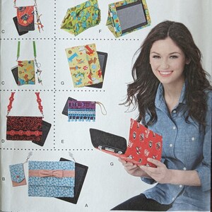 May include: Simplicity sewing pattern number 1339 OS, featuring a variety of tablet and phone cases. The pattern includes designs with different fabrics and embellishments, including a red case with a football team logo, a blue case with a bow, and a green case with a floral pattern. The pattern is designed and printed in the USA.