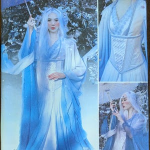 May include: Simplicity sewing pattern featuring a fantasy-themed dress with flowing blue fabric and a corset-style bodice. The pattern includes multiple views of the dress, showcasing its design details. The image also includes the text "Firefly Path" and "Since 1927".