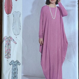 May include: A woman models a long, flowing, mauve dress with long sleeves and a round neckline. The dress is part of a Simplicity sewing pattern, with additional dress designs and the text "SOOIT A" and "Simplicity" visible.