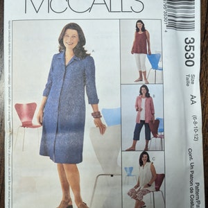 May include: McCall's sewing pattern envelope featuring a woman in a blue dress. The envelope includes images of different outfits, including a red top, a pink jacket, and a white top. The pattern size is AA (6-8-10-12).