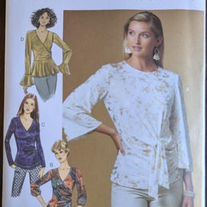 May include: Butterick B6628 sewing pattern featuring wrap tops with various sleeve styles. The pattern includes illustrations of the finished garments, showcasing different fabric and design options. The cover displays a woman wearing a white top with gold accents.