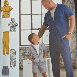 May include: Simplicity sewing pattern R11338 for a hooded jacket and pants. The pattern includes two sizes: S-L/S-XL and P-G/P-XG. The image shows a man and a child wearing the finished garments.