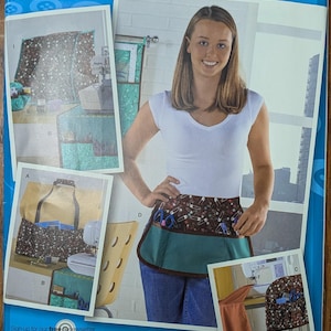 May include: A Simplicity 2679 Project Runway sewing pattern envelope featuring instructions for a multi-pocket apron, chair organizer, and storage bags. The cover displays a white t-shirt, blue jeans, and a brown and teal apron with safety pin prints.