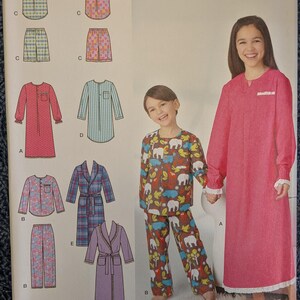 May include: A Simplicity sewing pattern envelope 1570 K5 for children's sleepwear in sizes 7-14. The cover displays illustrations of various pajama sets, nightgowns, and robes, alongside photographs of two children wearing the finished garments.
