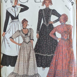 May include: A McCall's sewing pattern envelope, number 2056, featuring illustrations of four different long-sleeved dresses. The designs include a black dress with a white apron, a dark floral print dress, a light floral print dress, and a rust-colored floral dress.