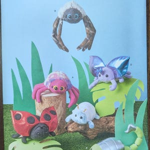 May include: Simplicity sewing pattern featuring plush insect toys, including a spider, butterfly, ladybug, and scorpion. The pattern includes the text "S3054" and "U.S. ONE SIZE". The toys are in various colors and sit on a green and brown background.