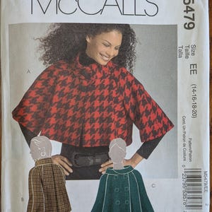 May include: McCall's sewing pattern M5479 for a cape in sizes EE (14-16-18-20). The envelope features a red and black houndstooth cape, a brown plaid cape, and a solid green double-breasted cape with buttons. The text includes the brand name.
