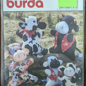 May include: A Burda pattern package featuring several soft toy cow designs. The package includes instructions for making cow plushies in two sizes, with the largest measuring approximately 13 3/4 inches. The cows are in various colors and patterns.