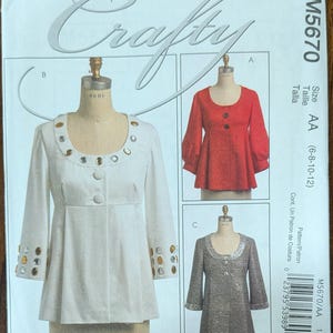 May include: McCall's Crafty sewing pattern M5670/AA. The pattern features three different top designs, including a white top with gold embellishments, a red top, and a silver-gray top. The size range is AA (6-8-10-12).