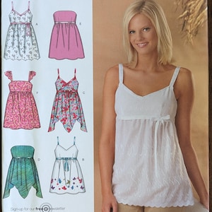 May include: Simplicity sewing pattern 4127 featuring six different top designs. The pattern includes sizes P5 (12, 14, 16, 18, 20). The image shows a woman wearing a white top. The text "Simplicity 6 made easy" is visible.