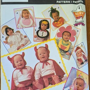 May include: A Simplicity Costumes sewing pattern envelope, number 7988, featuring illustrations of infants wearing various costumes including a devil, pumpkin, penguin, flower, and jester. The package includes HeatnBond branding and text.