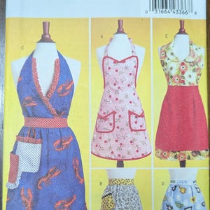 May include: Butterick B5474 sewing pattern featuring aprons in various styles. The aprons include a blue lobster print, a pink cherry print, and floral designs. The pattern includes sizes small, medium, and large.