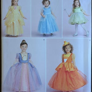 May include: Simplicity sewing pattern 1303 AA featuring children's princess costumes. The pattern includes designs for several dresses in various colors, including yellow, blue, green, and orange. The size range is 1/2-2.