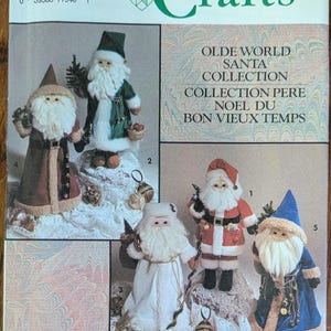 May include: A Simplicity Crafts sewing pattern envelope, number 7598, for an Olde World Santa collection. The front displays five distinct Santa Claus figures in various colored robes, including red, green, blue, brown, and white, each with a white beard.