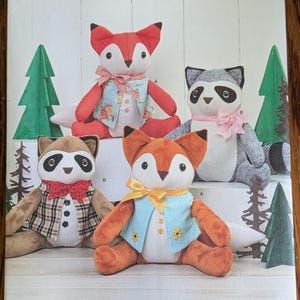 May include: Simplicity sewing pattern 8313 for stuffed animal toys. The package features illustrations of two foxes and two raccoons wearing vests and bows. The foxes are orange and white, while the raccoons are gray and brown. Text includes Simplicity 8313.