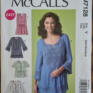 May include: McCall's M7128 sewing pattern envelope for a tunic with a scoop neckline and front slit. The pattern features four variations labeled A, B, C, and D, showcasing different sleeve lengths, fabric patterns, and lace trim details.