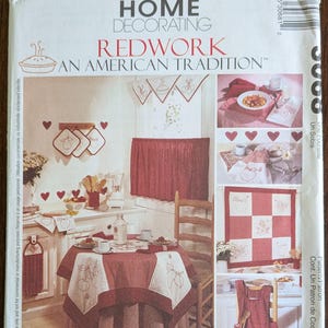 May include: A McCall's Home Decorating pattern featuring Redwork designs. The image showcases a kitchen scene with red and white textiles, including a tablecloth, curtains, and an apron. The text reads "Redwork: An American Tradition."