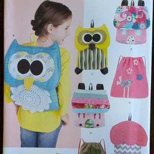 May include: Simplicity pattern featuring various children's backpack designs. The designs include owl, house, and tree shapes, with a girl modeling an owl backpack. The pattern includes the text "1602 OS" and "www.simplicity.com".