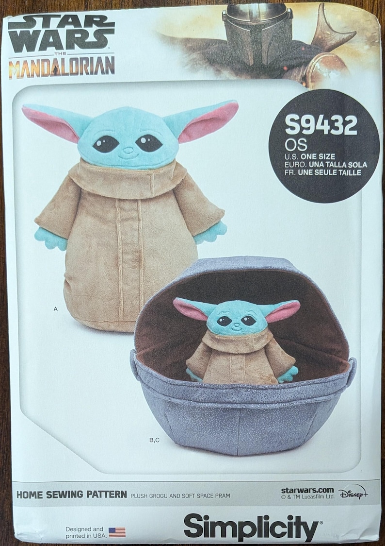 May include: A sewing pattern featuring a plush Grogu and soft space pram. The pattern includes a plush Grogu doll with blue skin, large ears, and a tan robe. The pram is a light blue color. The pattern is labeled "S9432 OS".