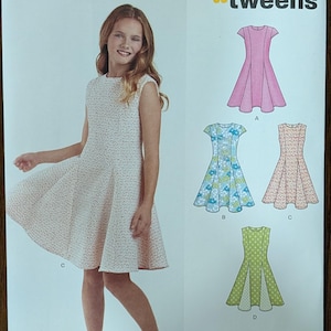 May include: New Look sewing pattern for tweens, featuring a girl modeling a sleeveless dress with a flared skirt. The pattern includes options for various dress styles, with the text "New Look" and pattern details visible.