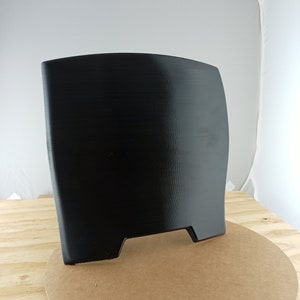 May include: A black plastic shield with a curved top and two small cutouts at the bottom. The shield is standing on a brown cardboard circle.