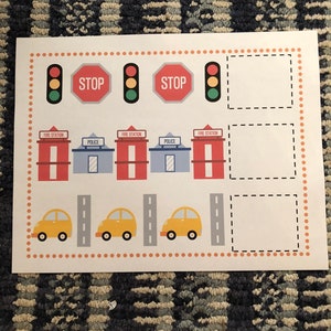 May include: A printable activity sheet for kids featuring a town scene with fire stations, police stations, traffic lights, stop signs, cars, and roads. The sheet includes blank spaces for drawing or writing.