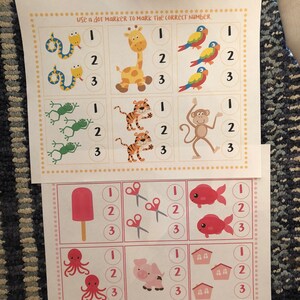 May include: A printable worksheet with colorful illustrations of animals, a popsicle, scissors, fish, an octopus, a pig, and houses. The worksheet is designed for children to count the number of items in each row and mark the correct number with a dot marker. The text "Use a dot marker to mark the correct number." is printed at the top of the worksheet.