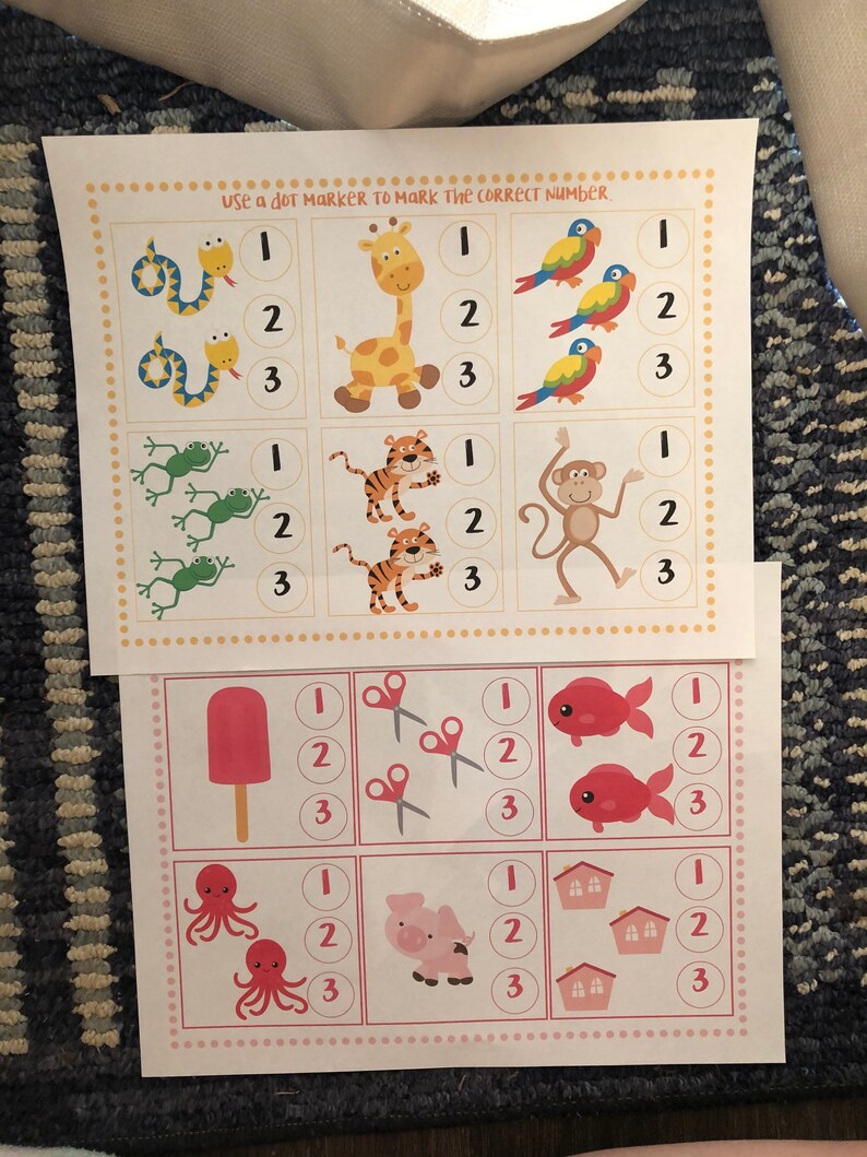 May include: A printable worksheet with colorful illustrations of animals, a popsicle, scissors, fish, an octopus, a pig, and houses. The worksheet is designed for children to count the number of items in each row and mark the correct number with a dot marker. The text "Use a dot marker to mark the correct number." is printed at the top of the worksheet.
