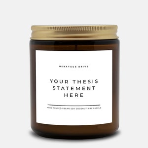 May include: A brown glass candle jar with a gold lid. The label reads "Herayus Drive" and "Your Thesis Statement Here". The bottom of the label reads "Hand Poured Vegan Soy Coconut Wax Candle".