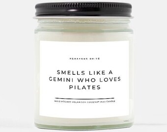 May include: A clear glass jar candle with a black lid. The label reads "Smells like a Gemini who loves Pilates".