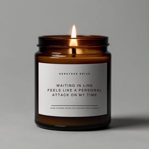 May include: A brown glass candle jar with a white label that reads "HERAYSUS DRIVE", "WAITING IN LINE", "FEELS LIKE A PERSONAL", "ATTACK ON MY TIME", and "HAND POURED VEGAN SOY COCONUT WAX CANDLE". The candle is lit.