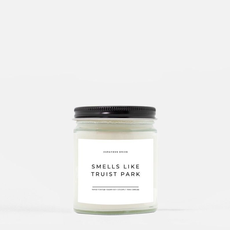 May include: A white candle in a clear glass jar with a black lid. The label reads "Smells Like Truist Park" and "Mercury Drive".